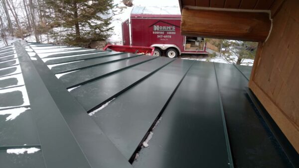 snow covered metal panels, with Michigan company Norm's Roofing in the background